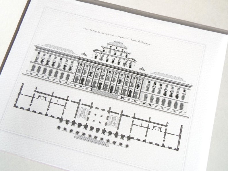 May include: Framed architectural print featuring a detailed black and white illustration of a building facade and a floor plan. The print is mounted on a white background and framed in a silver-tone frame. The text at the top reads "Suite des Bastides qui representent en premier un Ch&acirc;teau de Florence."