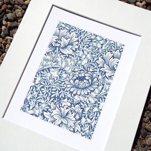 May include: A framed print featuring a blue and white floral pattern. The artwork showcases a detailed design of stylized flowers and foliage. The print is set within a white mat and frame, creating a clean, classic presentation. The overall aesthetic is reminiscent of vintage botanical illustrations.
