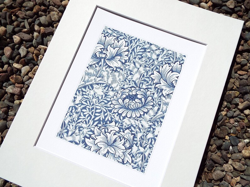 May include: A framed print featuring a blue and white floral pattern. The artwork showcases a detailed design of stylized flowers and foliage. The print is set within a white mat and frame, creating a clean, classic presentation. The overall aesthetic is reminiscent of vintage botanical illustrations.