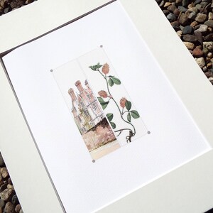 May include: A framed print featuring a watercolor illustration of a building with multiple chimneys and a sprig of clover. The artwork is matted in white and framed in a dark brown frame. The print is displayed on a white surface.