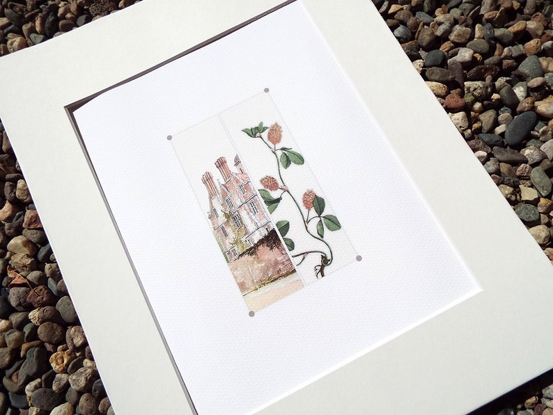 May include: A framed print featuring a watercolor illustration of a building with multiple chimneys and a sprig of clover. The artwork is matted in white and framed in a dark brown frame. The print is displayed on a white surface.