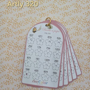 May include: A set of white arched cards held together by a gold metal ring with a small bee charm. Each card features a grid of flower outlines with printed numbers above them. The text reads Artly 320, Barbe à papa, and BeeColor by Laura.