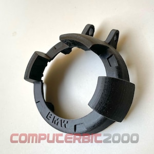 Op de afbeelding: Een zwart, 3D-geprint auto-onderdeel met de letters "BMW". Het cirkelvormige onderdeel heeft verschillende uitstekende secties en een getextureerd oppervlak. De tekst "COMPUTERBIC2000" staat onderaan.