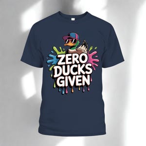 May include: Navy blue t-shirt featuring a cartoon duck wearing sunglasses and a backwards cap. The duck is surrounded by colorful paint splatters, with the text "ZERO DUCKS GIVEN" in a bold, dripping font.