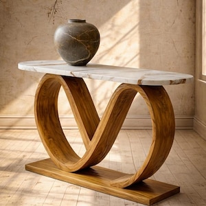 May include: A modern console table with a white marble top and a unique wooden base. The base features a continuous, flowing design. A decorative, round, dark-colored vase sits on the table's surface. The table is set in a room with natural light.