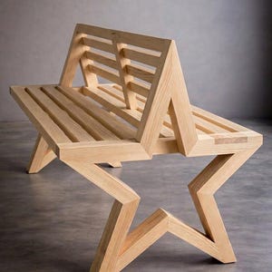Puede incluir: Un banco de madera con forma de estrella. El banco está hecho de madera clara y tiene un asiento y respaldo de listones. Las patas y el marco son angulares, creando una estética geométrica única. El banco es un mueble.