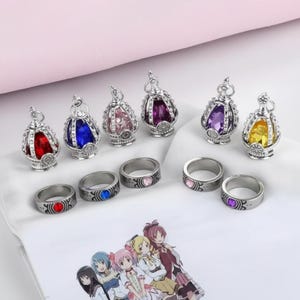 May include: A collection of silver-toned rings and pendants with colorful gemstone accents. The pendants are crown-shaped, and the rings feature matching colored stones. The gemstones are red, blue, pink, purple, and yellow.