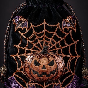 Könnte beinhalten: Schwarzer Samt-Kordelzugbeutel mit Halloween-Stickerei. Mit einem Kürbis, Spinnennetz und Fledermäusen aus orangefarbenen und lila Pailletten. Die Tasche hat einen Perlenkordelzug und Quastenakzente.