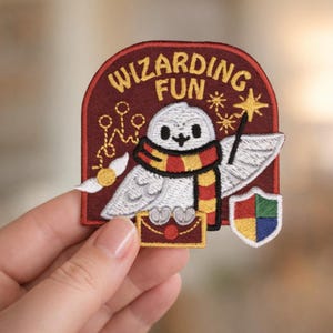 May include: Embroidered patch featuring a white owl wearing a scarf with red and yellow stripes, holding a wand. The patch includes the text "WIZARDING FUN" in gold lettering, a golden snitch, and a shield with four colored sections.