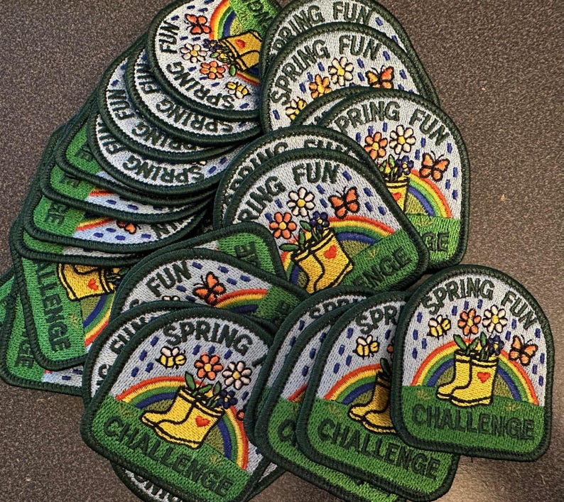 May include: A collection of embroidered patches with a spring theme. Each patch features a rainbow, yellow rain boots, flowers, and butterflies. The text "SPRING FUN CHALLENGE" is included on each patch, with a green border.