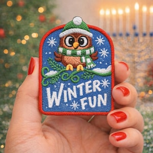 May include: Embroidered patch featuring a brown owl wearing a green and white scarf and hat. The patch has a blue background with white snowflakes and the words "Winter Fun". A festive winter-themed accessory.