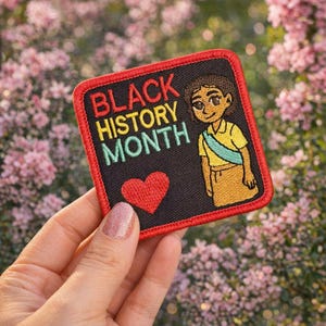 May include: Embroidered patch with the text "BLACK HISTORY MONTH" in red, yellow, and green. The patch features a cartoon illustration of a person and a red heart on a black background, framed by a red border.