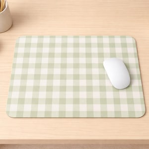Puede incluir: Un tapete de ratón a cuadros verde claro y blanco con un ratón de computadora blanco sobre un escritorio de madera clara. Un pequeño cuenco blanco con clips dorados y una taza de cerámica blanca con lápices también están en el escritorio.