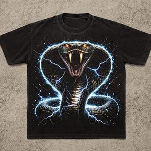 May include: Black t-shirt featuring a detailed graphic of a cobra with its hood flared, surrounded by blue lightning bolts. The cobra has orange eyes and sharp fangs. The shirt is a classic crew neck style.