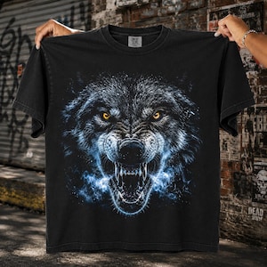 May include: A black short-sleeve t-shirt featuring a large, detailed graphic of a snarling wolf face. The wolf has intense glowing yellow eyes, sharp bared teeth, and is surrounded by wisps of blue energy or smoke emanating from its open mouth.