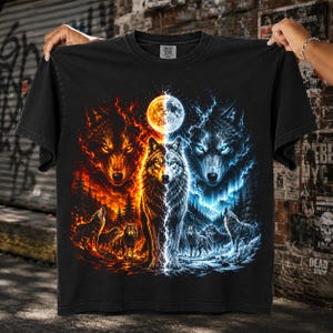 Puede incluir: Una camiseta negra de manga corta con un estampado gráfico de lobos. El diseño muestra un lobo central dividido entre tonos naranja ardiente y azul gélido, con una luna arriba y lobos más pequeños en un paisaje forestal debajo.