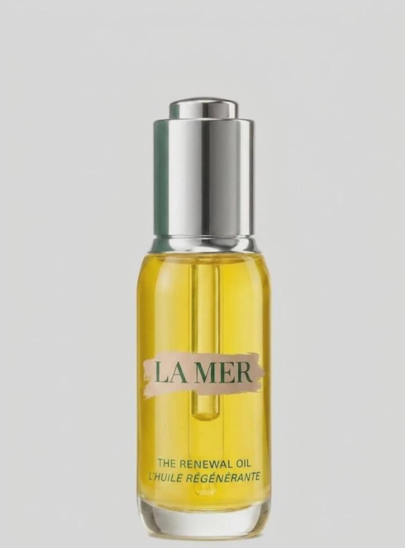 May include: A clear glass bottle filled with golden yellow oil, featuring a silver dropper cap. The label displays the text LA MER, THE RENEWAL OIL, and L'HUILE R&Eacute;G&Eacute;N&Eacute;RANTE in dark green lettering over a light beige brushstroke background.