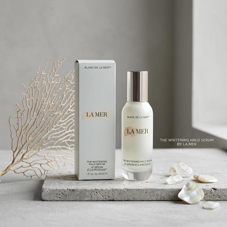 May include: A La Mer Blanc de La Mer The Whitening Halo Serum bottle and its matching rectangular box. The white bottle has a silver cap and contains 30 ml of serum. The box displays the text Blanc de La Mer, La Mer, and The Whitening Halo Serum.