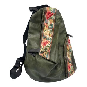 May include: Olive green backpack with floral embroidery. The bag has a black adjustable shoulder strap, a front zip pocket, and a decorative embroidered panel with red and yellow flowers. The bag has a leather-like texture and a zip closure.