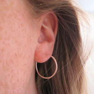 May include: A close-up of a person's ear with a silver hoop earring. The earring is simple and understated, and it is a classic style that can be worn with any outfit.