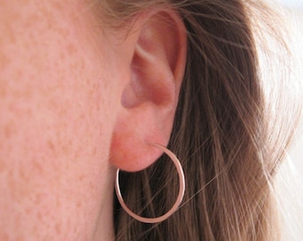 May include: A close-up of a person's ear with a silver hoop earring. The earring is simple and understated, and it is a classic style that can be worn with any outfit.