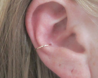 May include: A close-up of a person's ear with a small, gold, hammered hoop earring in the upper cartilage.