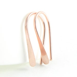 May include: A pair of rose gold hoop earrings with a simple, curved design. The earrings are made of a thin wire and have a smooth, polished finish.