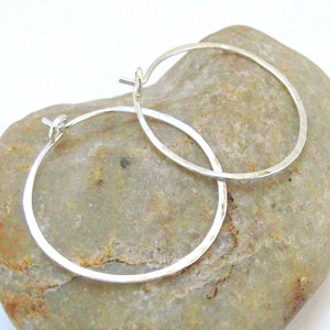May include: A pair of silver hoop earrings with a hammered finish. The earrings are simple and elegant, and they would make a great gift for any occasion.