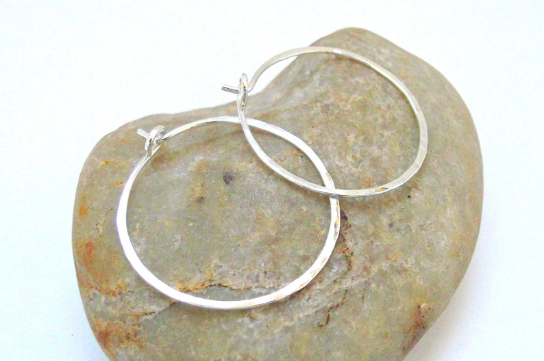 May include: A pair of silver hoop earrings with a hammered finish. The earrings are simple and elegant, and they would make a great gift for any occasion.