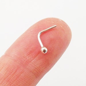 May include: A silver nose ring with a small ball at the end. The ring is bent at a 90-degree angle.