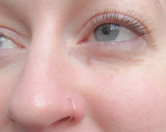 May include: Close-up of a person's face with a small gold nose ring.