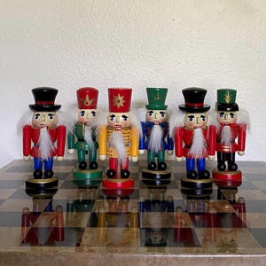 May include: A collection of six wooden nutcracker figurines standing in a row. Each figure wears a distinct uniform in shades of red, green, blue, yellow, and black, featuring painted facial details, white faux fur beards, and tall hats.