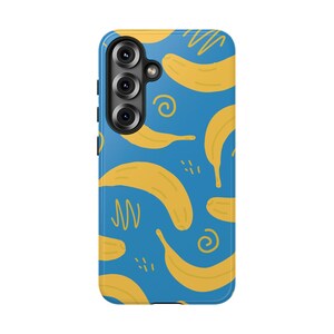 May include: A blue smartphone case featuring a repeating pattern of yellow bananas interspersed with small yellow scribbles, swirls, and dash marks. The case has a cutout for a triple-lens camera system on the upper left side with black circular lenses.