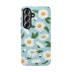 May include: A light blue phone case featuring a repeating pattern of white daisies with yellow centers and green leaves. The case has a camera module on the upper left side.