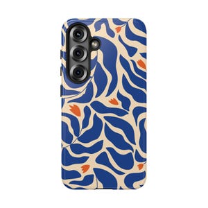 May include: A rectangular mobile phone case featuring a repeating pattern of dark blue organic leaf shapes and small orange flower buds on a light cream background, with a triple camera cutout located in the upper left corner of the device.