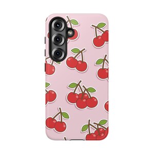 May include: A light pink smartphone case featuring a repeating pattern of red cherries with green leaves. The case has a black camera module cutout in the upper left corner with three circular lenses arranged vertically on the back surface.