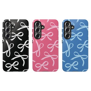 May include: Three phone cases with bow patterns. One case is black with white bows, another is pink with white bows, and the third is blue with light blue bows. Each case has a camera module.