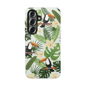 Può includere: Una cover per smartphone bianca con un motivo ripetuto di tucani dal becco arancione, foglie tropicali di palma e monstera verdi e fiori di plumeria giallo pallido. La cover presenta un ritaglio verticale per la fotocamera.