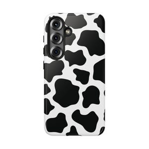 May include: A white smartphone case with a black cow print design. The case has a glossy finish and a camera module with three lenses. The cow print pattern consists of irregular black spots on a white background, creating a bold and playful aesthetic.