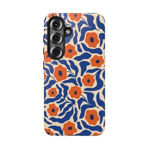 May include: A phone case with a floral pattern. The case features a cream-colored background with a repeating design of orange flowers and blue leaves. The phone case has a camera module with three lenses.