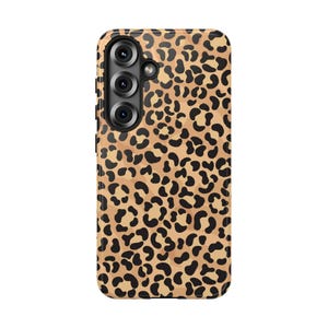 May include: A phone case with a leopard print design. The case features a tan background with black spots, and a camera module with three lenses. The case is designed to protect the phone from scratches and damage.