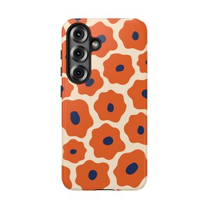 May include: A phone case featuring a repeating pattern of orange flower shapes with navy blue centers on a cream background. The case has a camera module on the upper left.