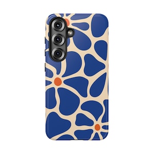 May include: A rectangular smartphone case featuring a repeating pattern of large, rounded blue flower petals on a cream background. Each flower has a small, solid orange center. The case includes a vertical cutout for a triple-lens camera system.