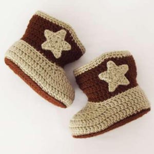 May include: A pair of handmade crochet baby boots. The boots are brown and tan with a star applique on the side. The boots are made of soft yarn and are designed to keep a baby's feet warm.