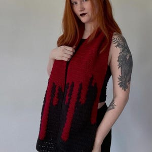 Könnte beinhalten: Handgefertigter Häkelschal mit auffälligem Design. Der obere Teil ist leuchtend rot, der in eine schwarze Basis mit roten Tropfen übergeht. Der Schal ist ein einzigartiges Accessoire, perfekt, um jedem Outfit ein kühnes Statement zu verleihen. Ca. 150 cm lang.