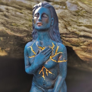 May include: A blue ceramic sculpture of a woman kneeling with her hands clasped in front of her chest. The sculpture has gold paint details on the chest area, resembling branches or roots.