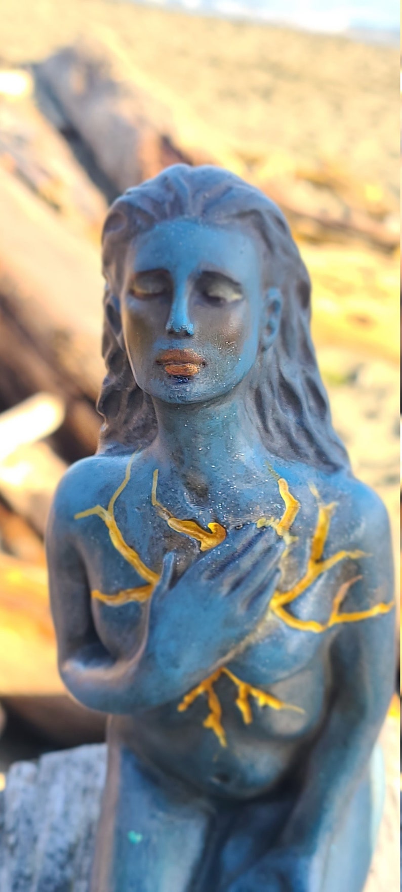 May include: A blue statue of a woman with her hands clasped over her heart. The statue has gold accents on the chest and hair.