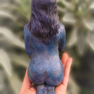 May include: A blue ceramic figurine of a person sitting with their back to the viewer. The figurine has a detailed face and hair, and is painted in a blue and purple color scheme.