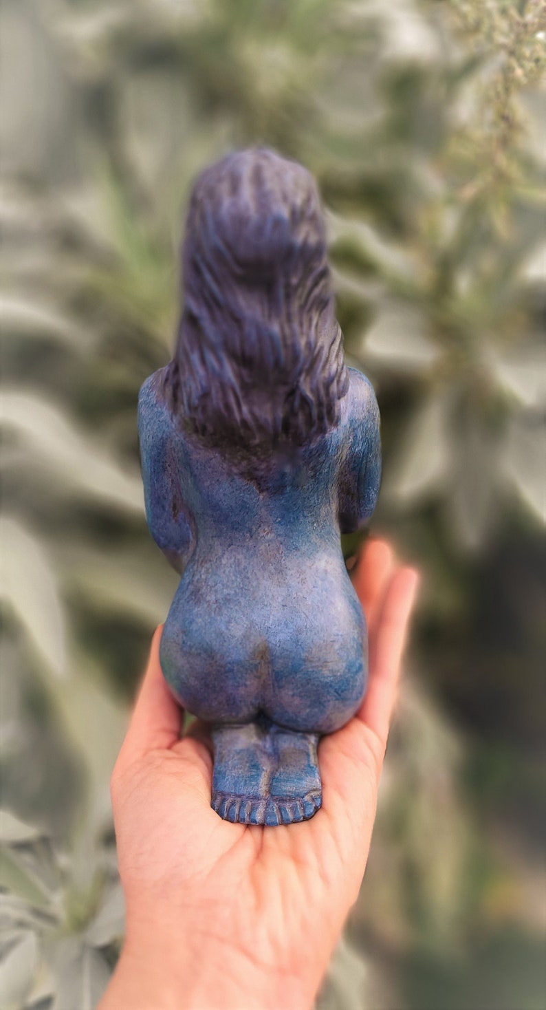 May include: A blue ceramic figurine of a person sitting with their back to the viewer. The figurine has a detailed face and hair, and is painted in a blue and purple color scheme.