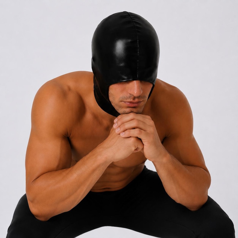 May include: A black hood made of a shiny material. The hood covers the head and neck, with an opening for the face. The hood is worn by a person. The person is wearing black pants.